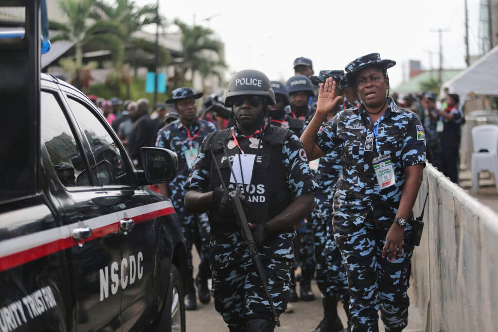 Nigerian security personnel in camo uniforms next to their vehicle during an event.