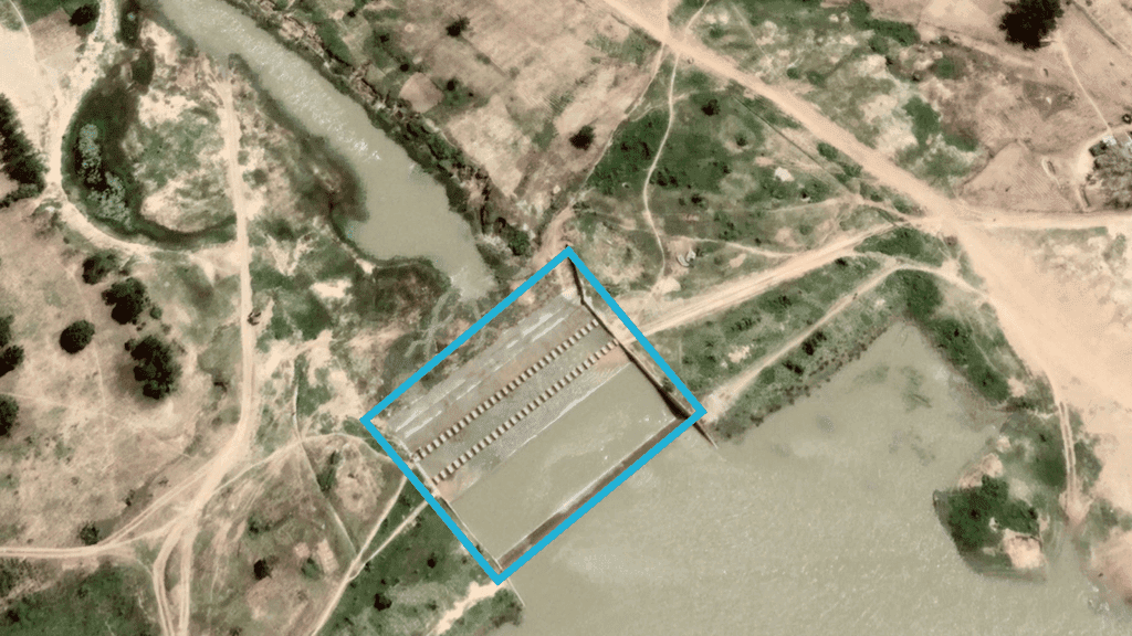 Aerial view of an aquaculture farm near a river, with rectangular ponds and access paths.