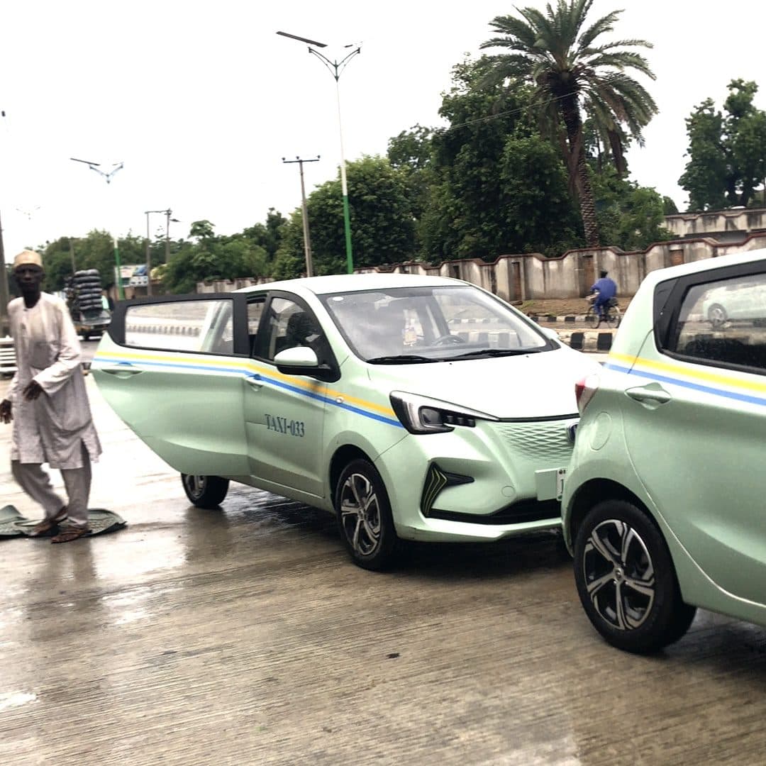 A man walking past colorful taxis on a wet street lined with palm trees.
