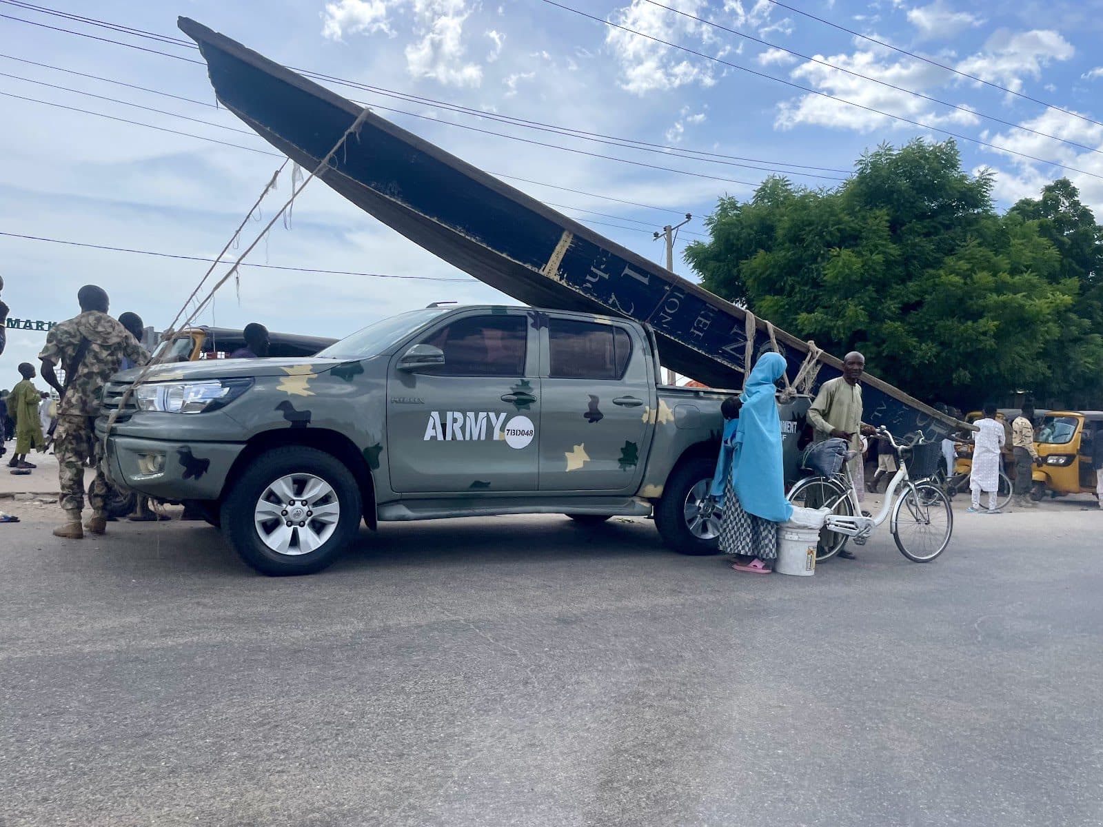 Army vehicle and civilians on a busy street with an overturned billboard in the background.