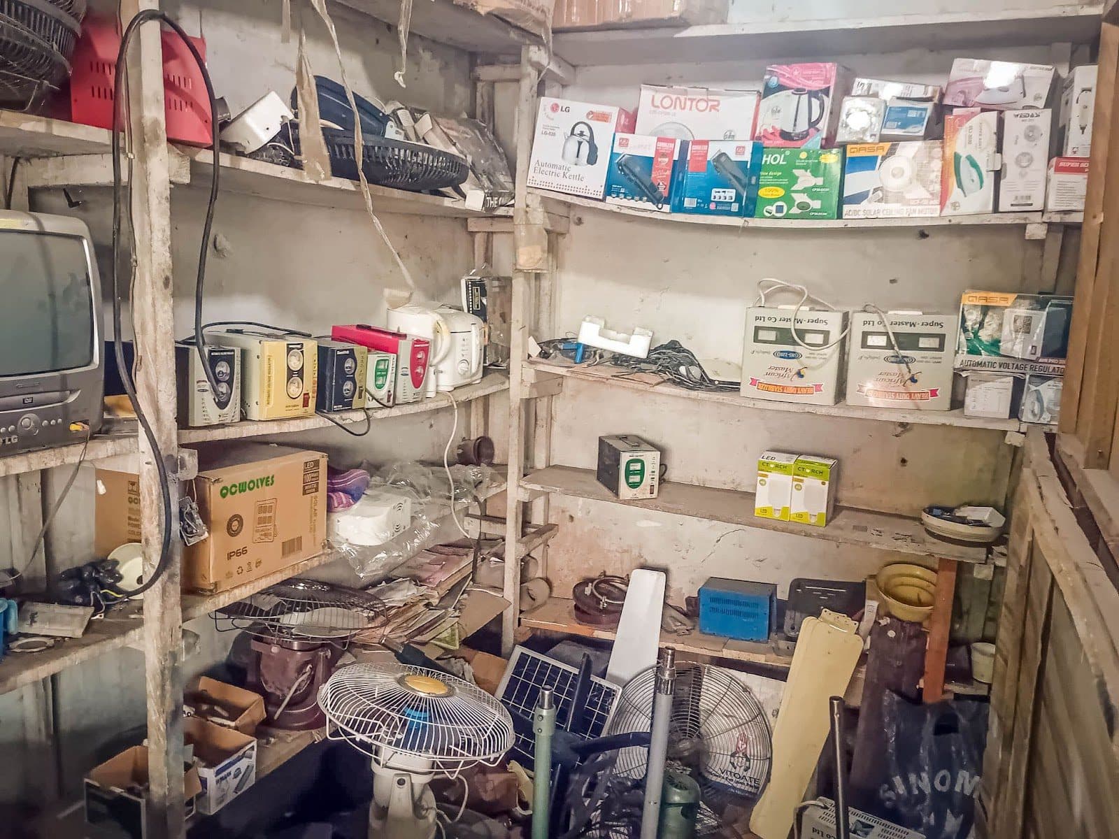An overcrowded storage room with various electronic items and boxes on shelves.