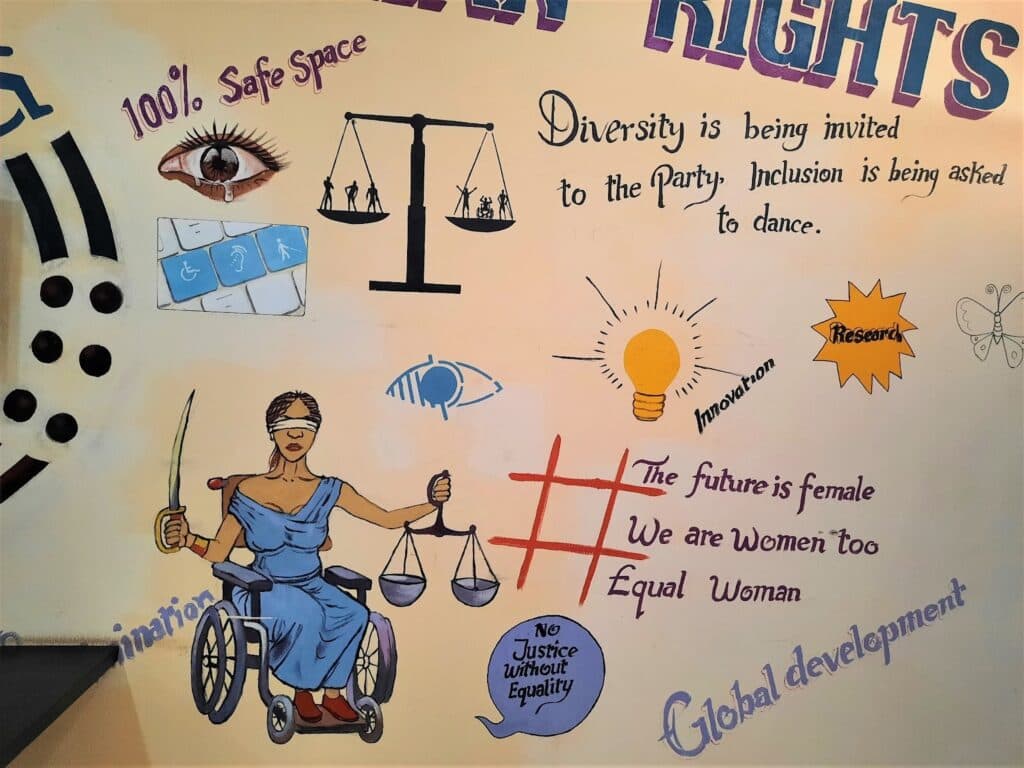 Wall mural with symbols of diversity, inclusion, and female empowerment, including Justice Lady in a wheelchair.