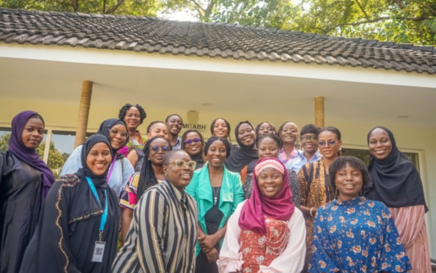 A diverse group of smiling women gathered for a group photo outdoors.