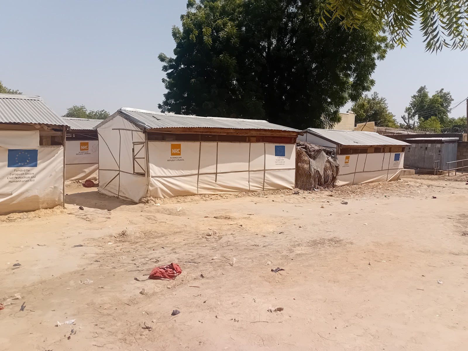 Aid tents with EU and NRC logos in a dry, sandy area with sparse vegetation.