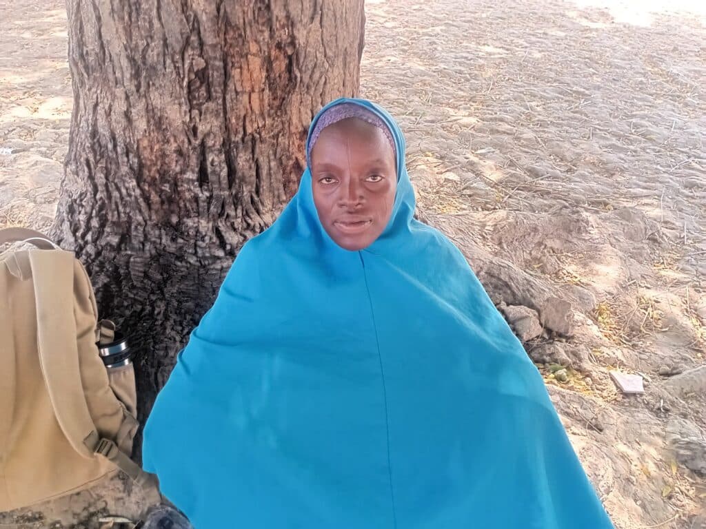 Woman in blue shawl sitting by a tree with a thoughtful expression.