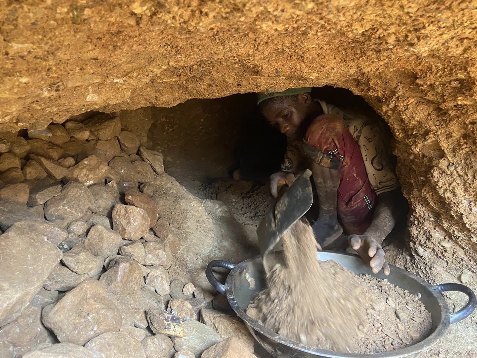 Person in a tunnel shoveling earth into a pan, surrounded by dirt and rocks.