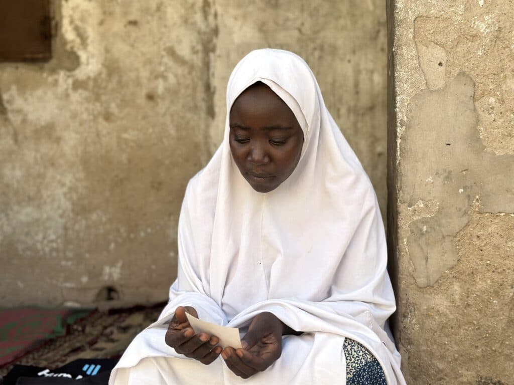 Woman in white hijab sitting and reading a note outdoors.