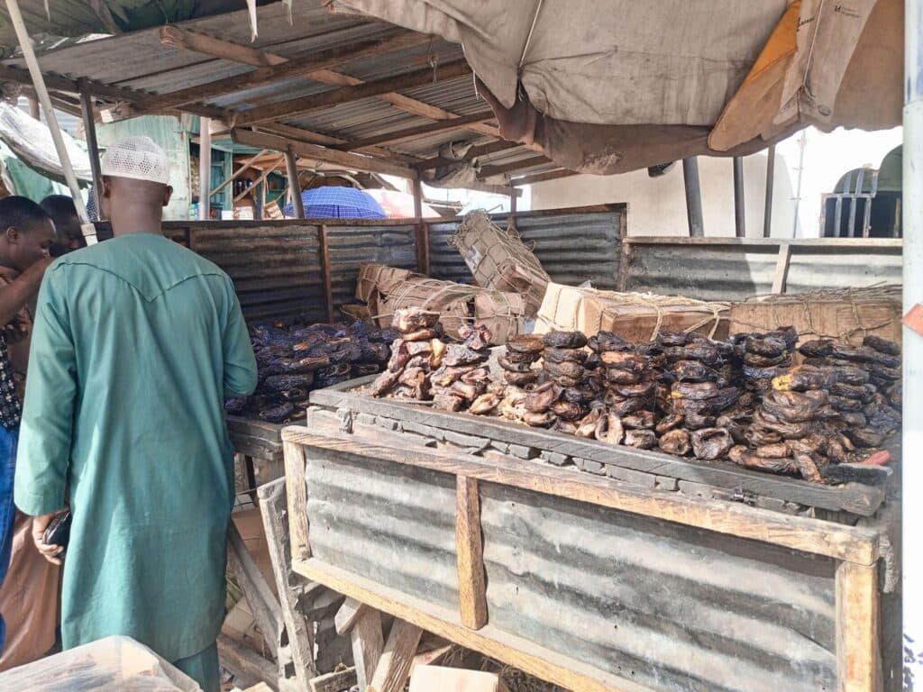 Street market scene with people browsing dried fish on wooden stalls.