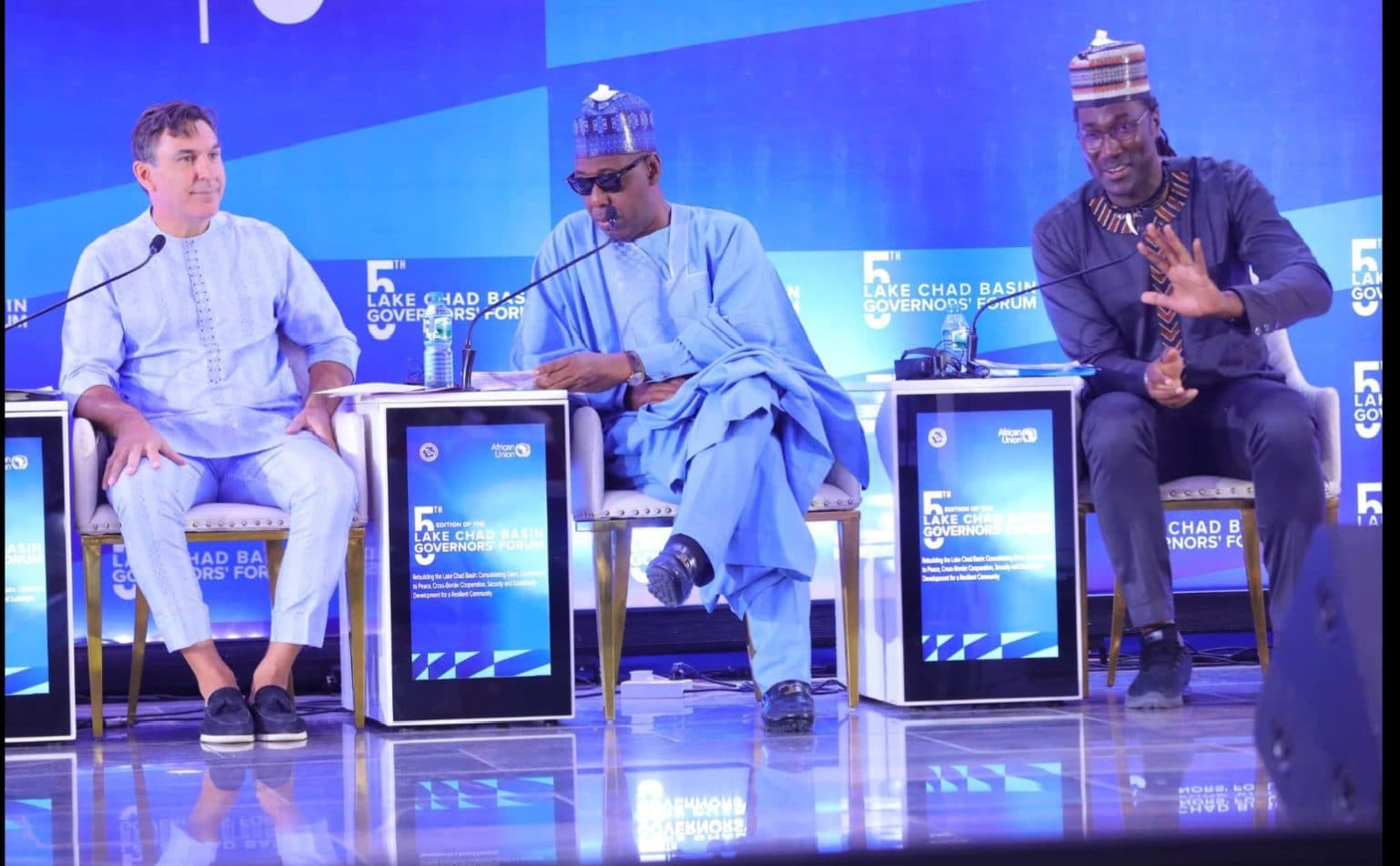 Three men on stage at the 5th Lake Chad Basin Governors' Forum, with blue-themed backgrounds and event branding.