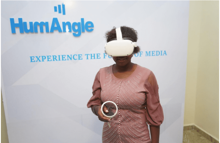 Person using a VR headset and controller in front of a "HumAngle" and "Experience the Future of Media" sign.