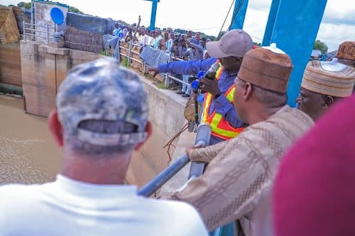 Group of people gathered at a water control structure, with one person pointing towards the water.
