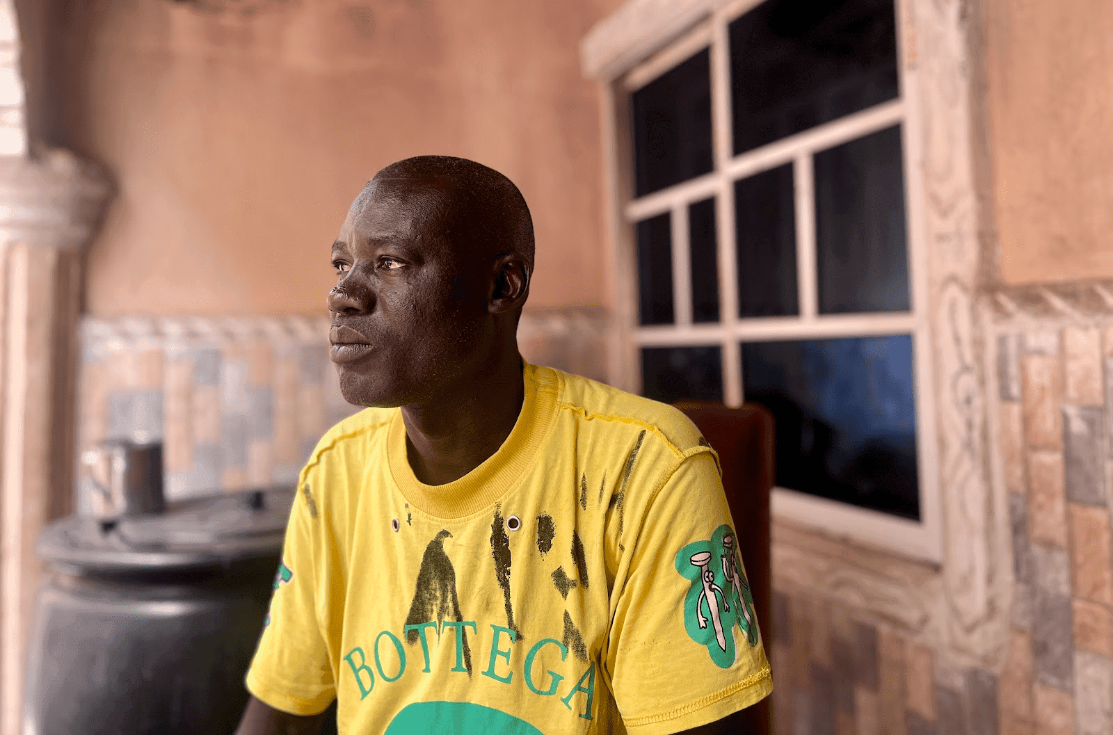 Man in a yellow T-shirt sits indoors, looking to the side.
