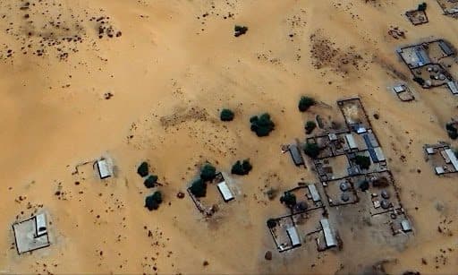 Aerial view of a small village with scattered buildings and sparse vegetation in a desert landscape.