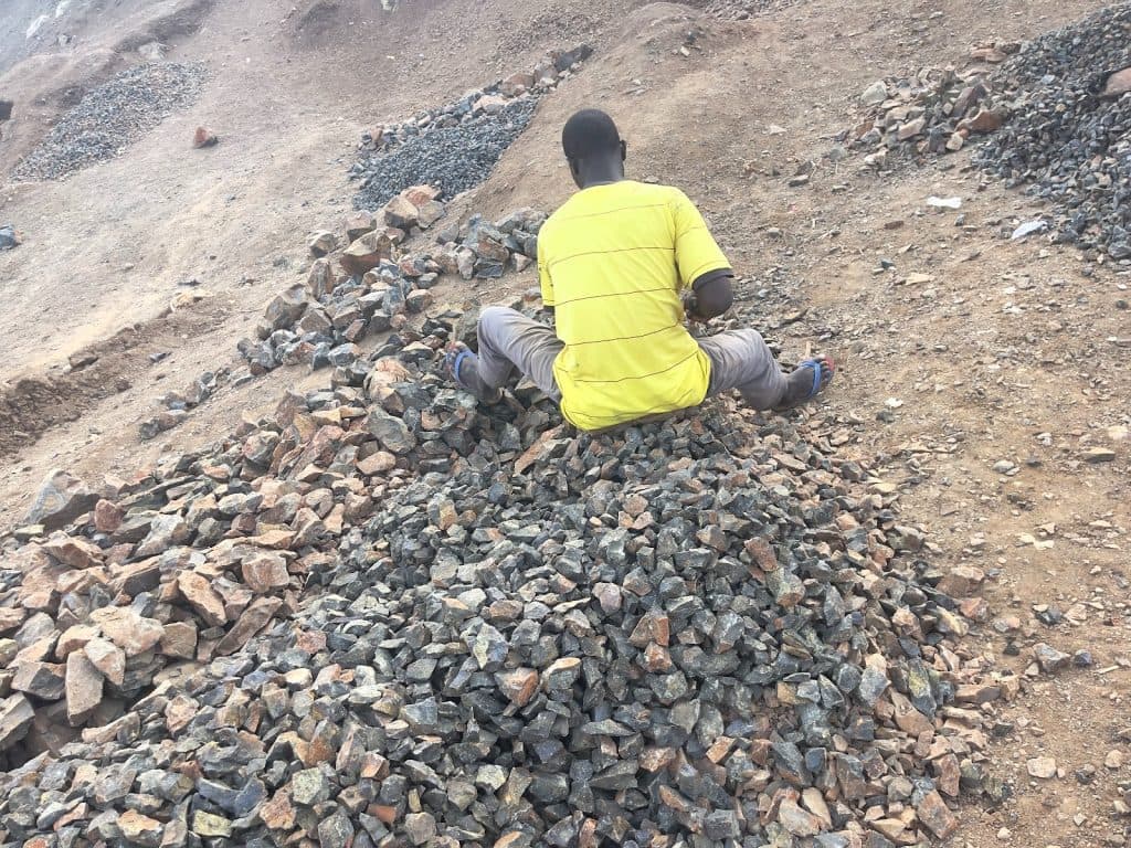 Person in a yellow shirt sitting on a pile of rocks in a rocky, barren landscape.