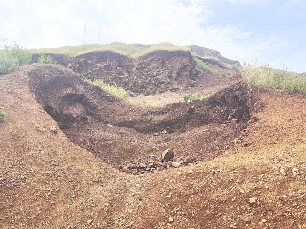 Eroded rocky terrain with green plants under a blue sky.