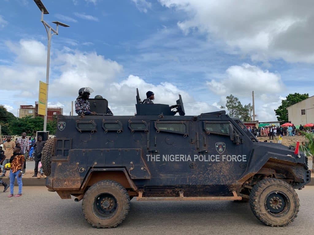 Armored vehicle of the Nigeria Police Force on a sunny street surrounded by people.