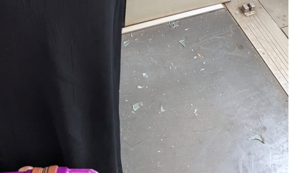 Broken glass pieces on a train floor near a black curtain and a person