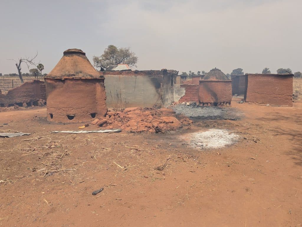 Rural scene with traditional clay kilns and burnt ground under a hazy sky. Sparse trees and dry earth in the background.