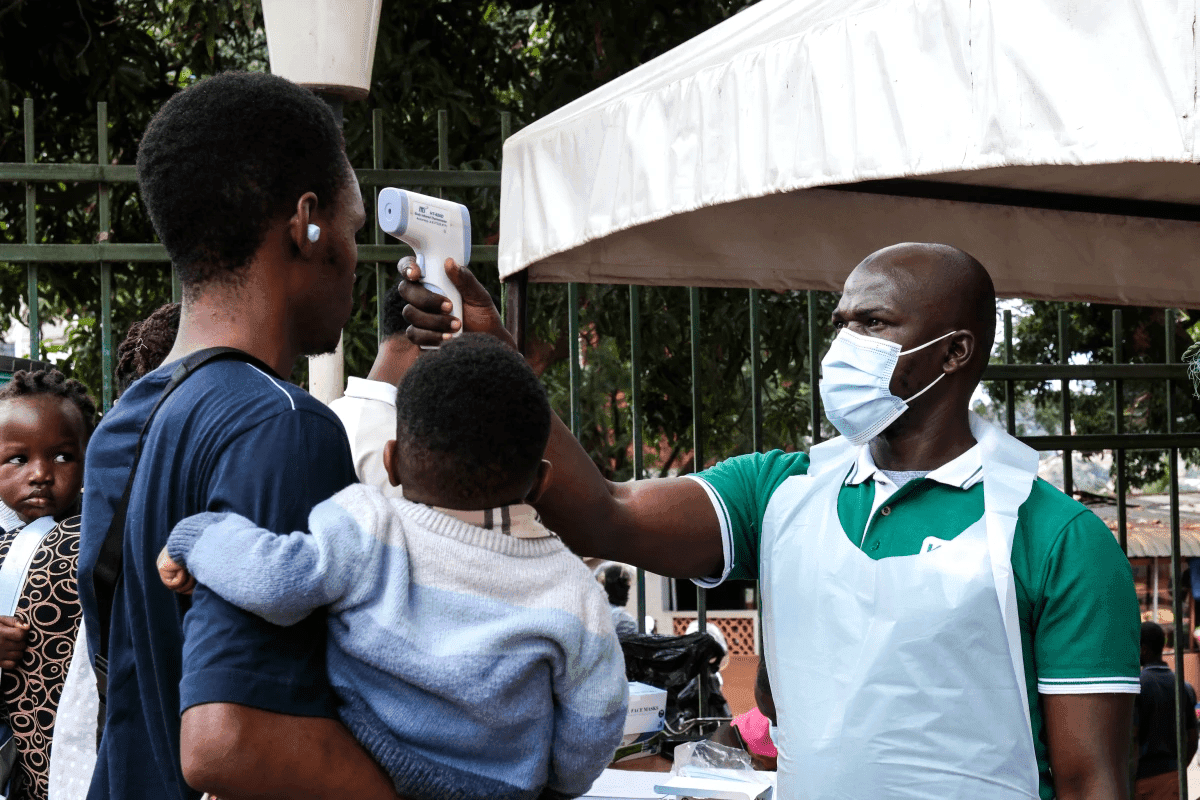 A person having their temperature checked with an infrared thermometer by a masked healthcare worker. A child is held by the person.