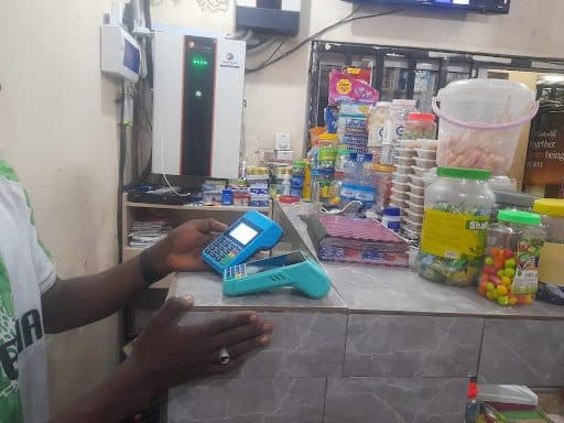 Person holding a POS device at a store counter, surrounded by various products.